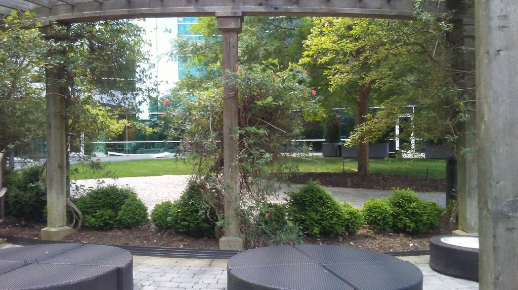A courtyard with trees and bushes in the background and seating in the foregrount